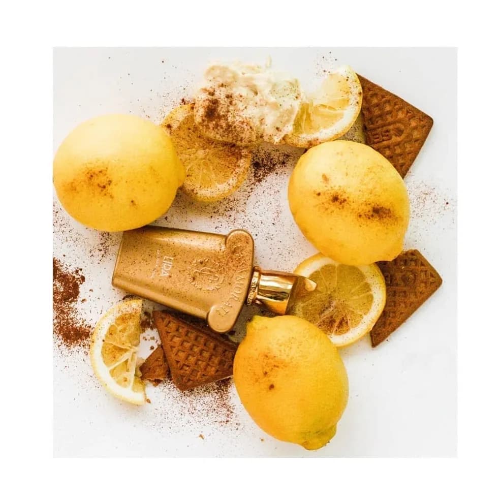 Gold perfume bottle on a white surface with lemons, biscuits and cinnamon dust