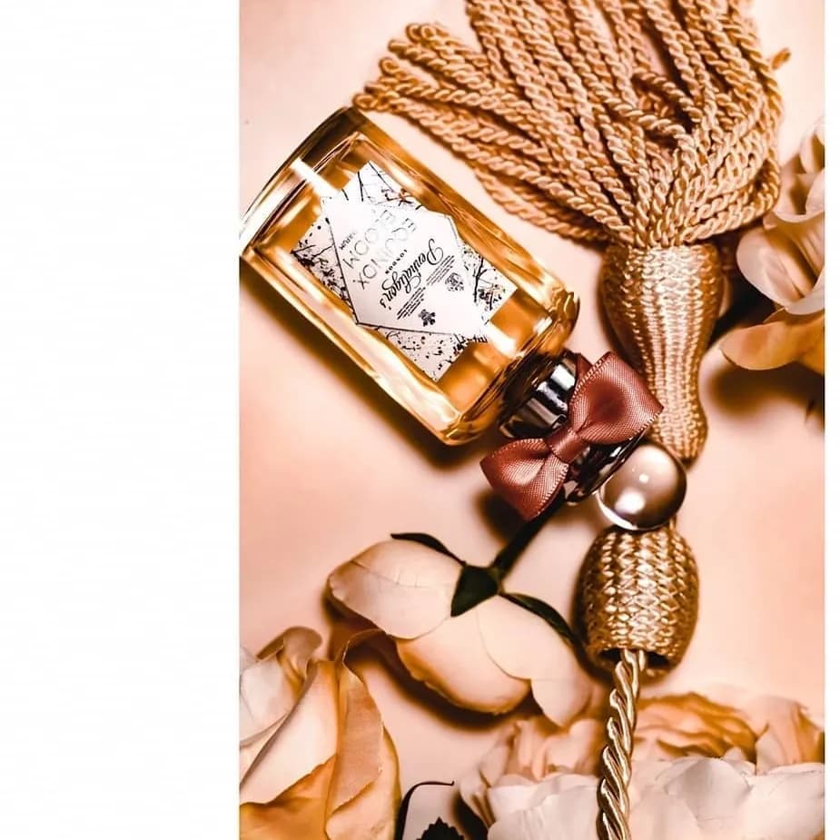 Warm-toned bottle on blush silk with a gold tassel and rose petals